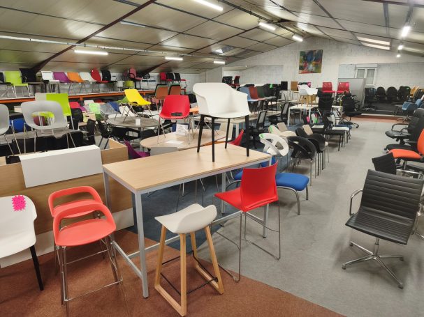 Salle remplie de chaises colorées et de tables variées dans un espace de vente.