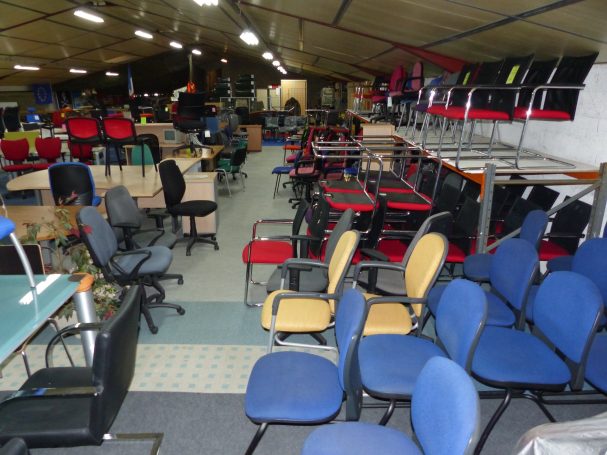 Salle de stockage avec de nombreuses chaises et bureaux de différents styles et couleurs.