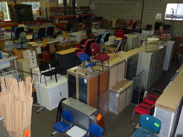 Entrepôt rempli de meubles et de chaises de bureau, organisé avec des allées étroites.