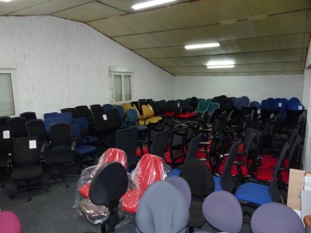Salle remplie de chaises de bureau, certaines empilées, dans un espace éclairé.