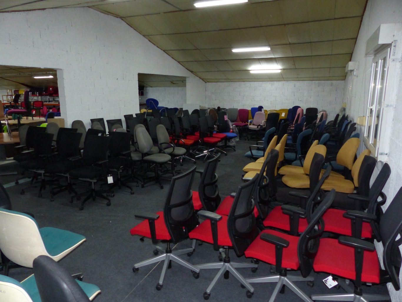 Salle remplie de chaises de bureau variées, en cuir et en tissu, sur un sol sombre.