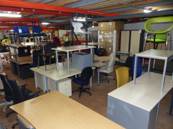 Bureaux et chaises empilés dans un espace de travail encombré.